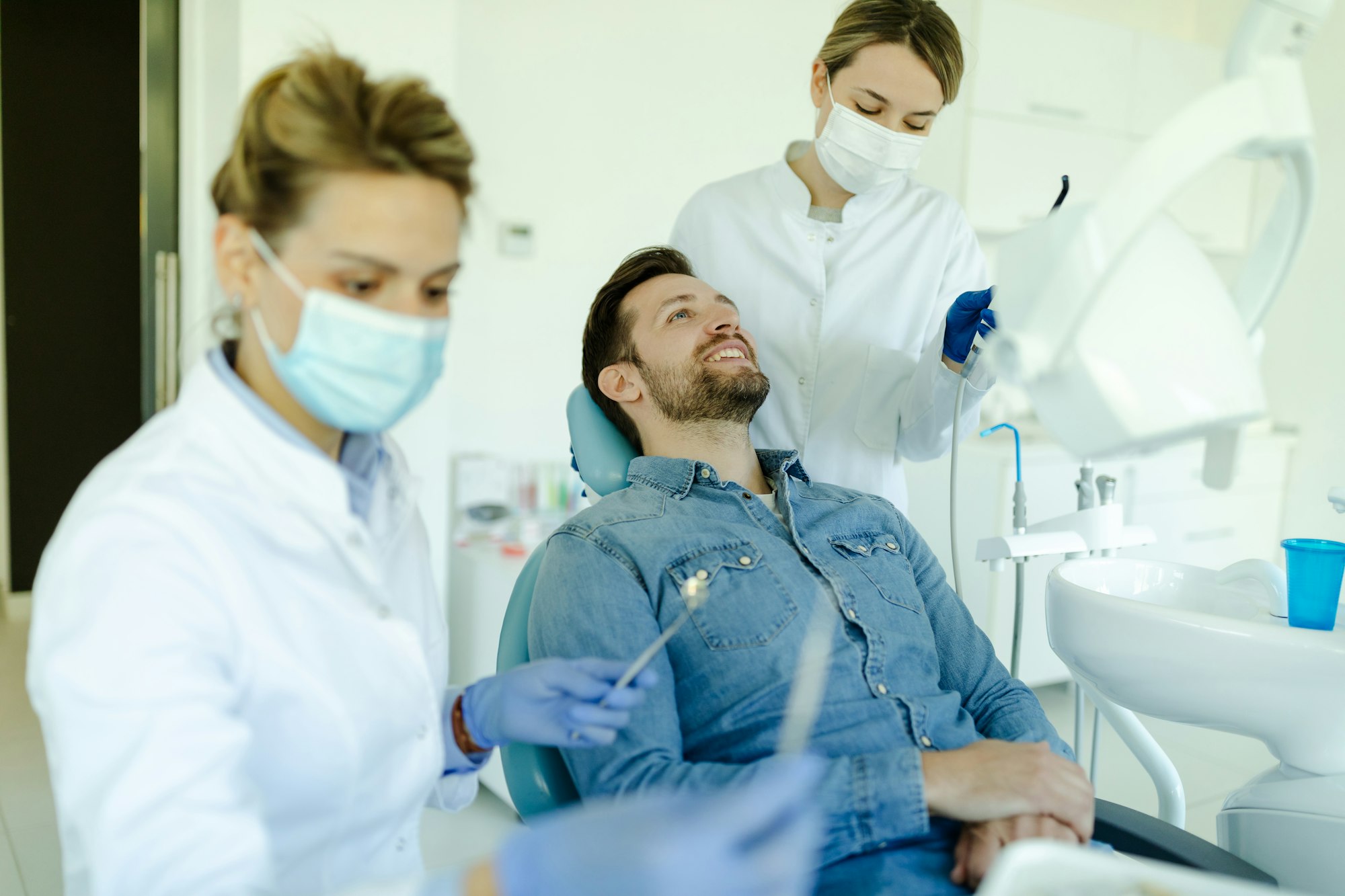 Female dentist with assistant preparing instrument for dental examination in the dentist office.